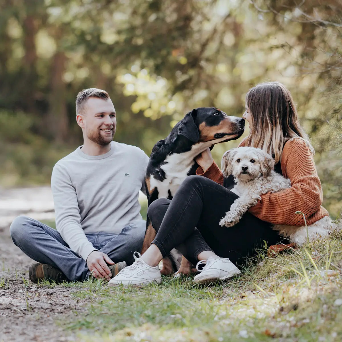 Coppia felice seduta a terra nella foresta con i loro due cani che si coccolano.