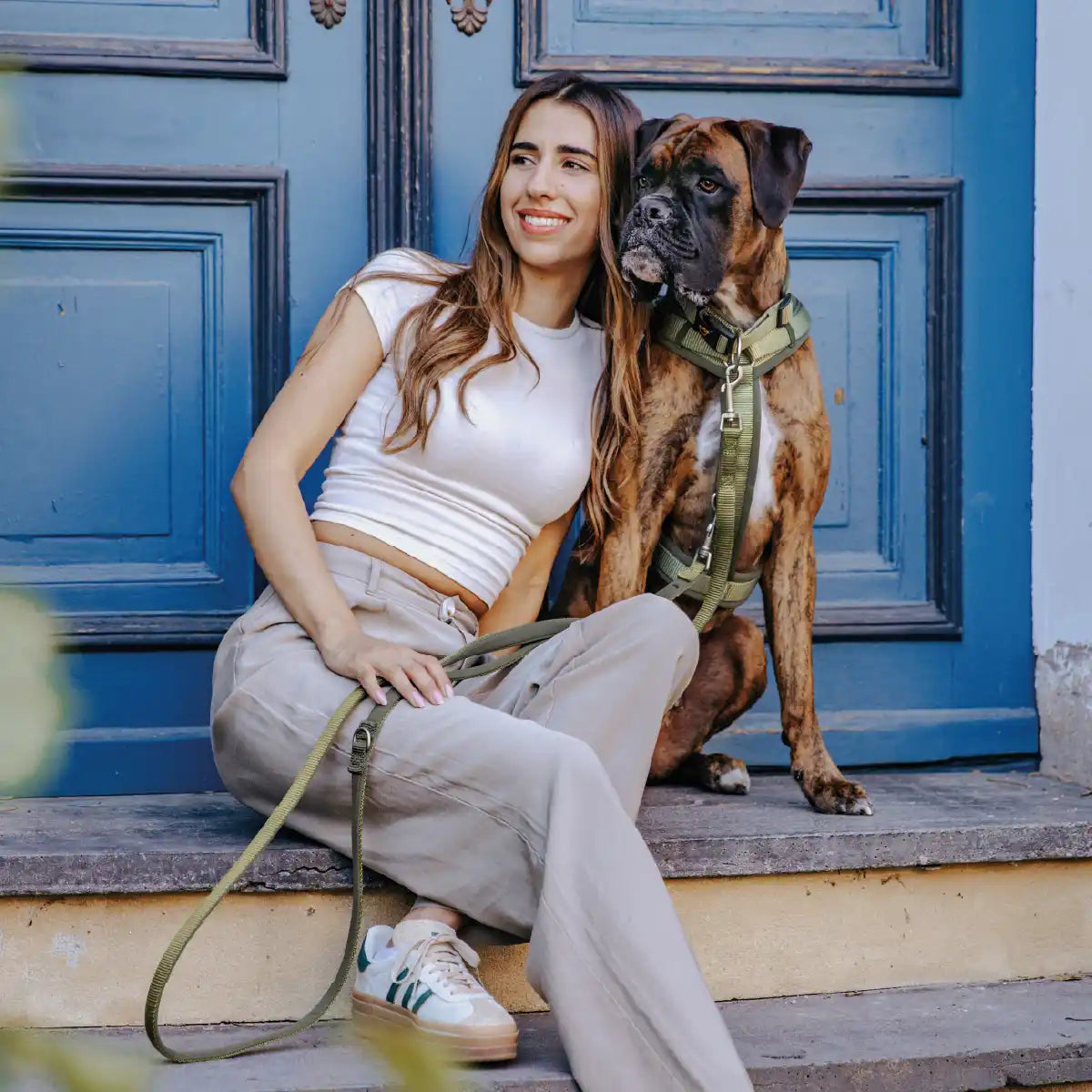 Frauchen sitzt mit ihrem Hund auf einer Stufe vor einer Tür und der Hund trägt Rudelkönig Geschirr Bella und Halsband Bella.
