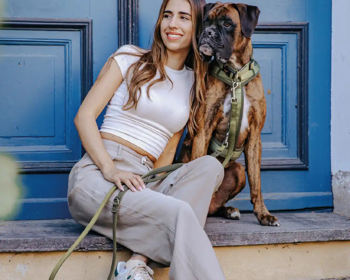 Frauchen sitzt mit ihrem Hund auf einer Stufe vor einer Tür und der Hund trägt Rudelkönig Geschirr Bella und Halsband Bella.