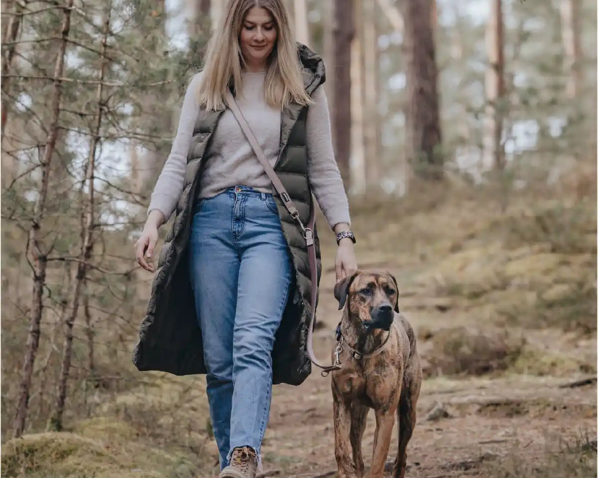 Frauchen geht mit ihrem Hund und der Rudelkönig Umhängeleine Paola im Wald spazieren.