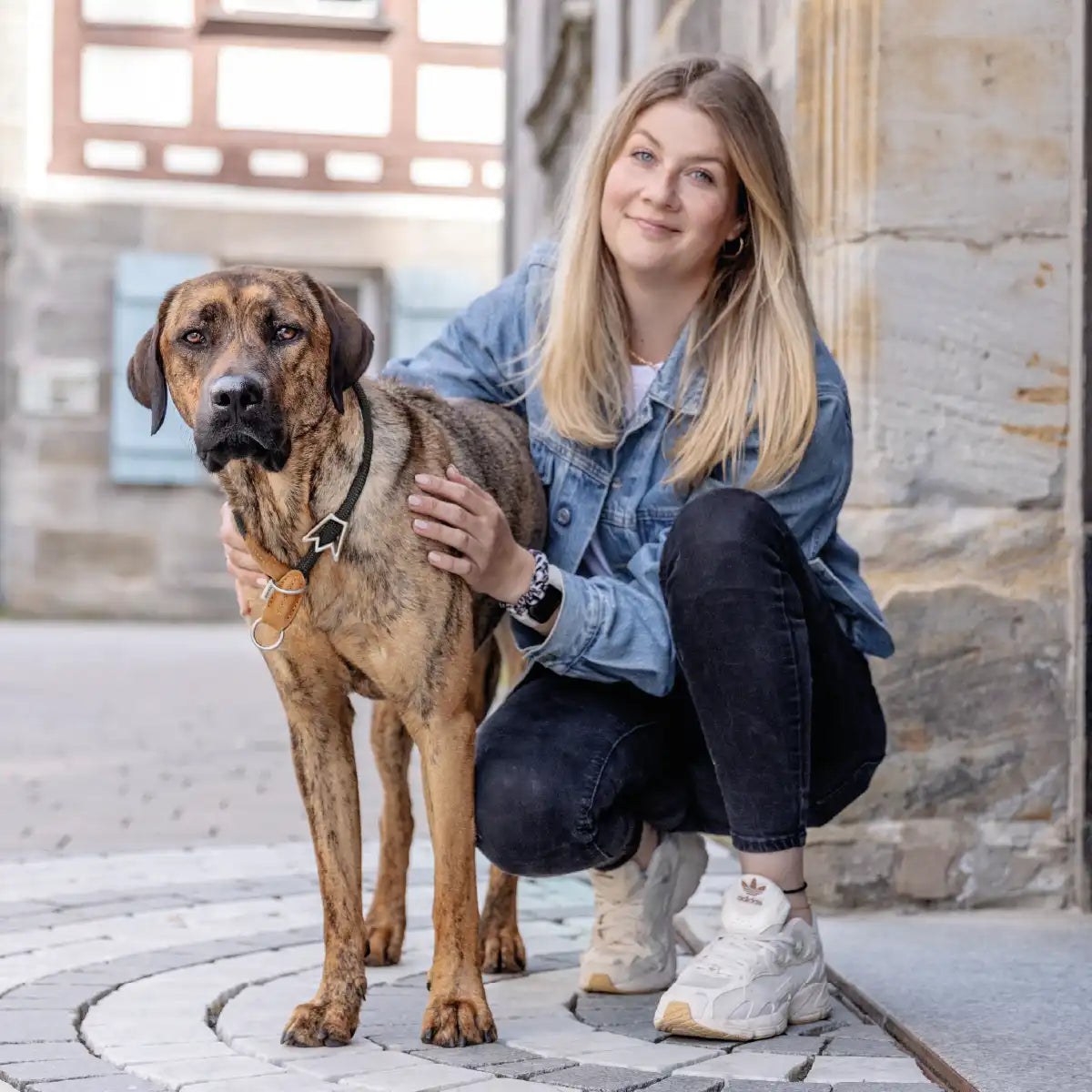 Frauchen steht kniet mit ihrem Hund und dem Rudelkönig Zugstophalsband Emma in der Stadt und beide schauen in die Kamera.