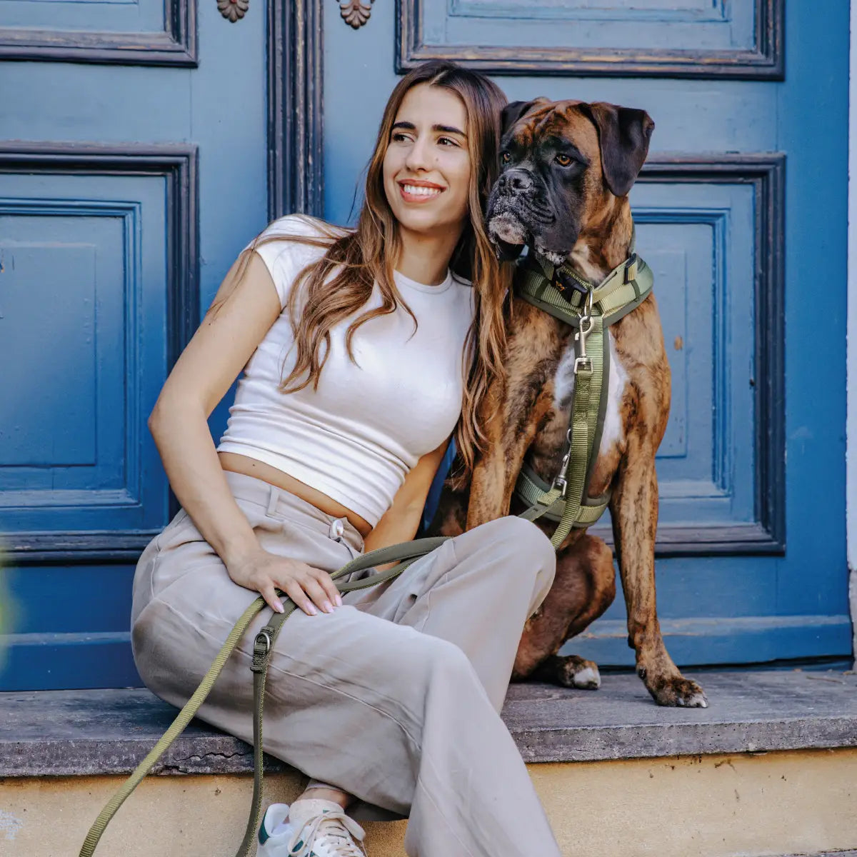 Boxer sitzt mit seiner Halterin entspannt auf einer Stufe, das grüne Hundehalsband von Rudelkönig gut sichtbar – funktional & modern.