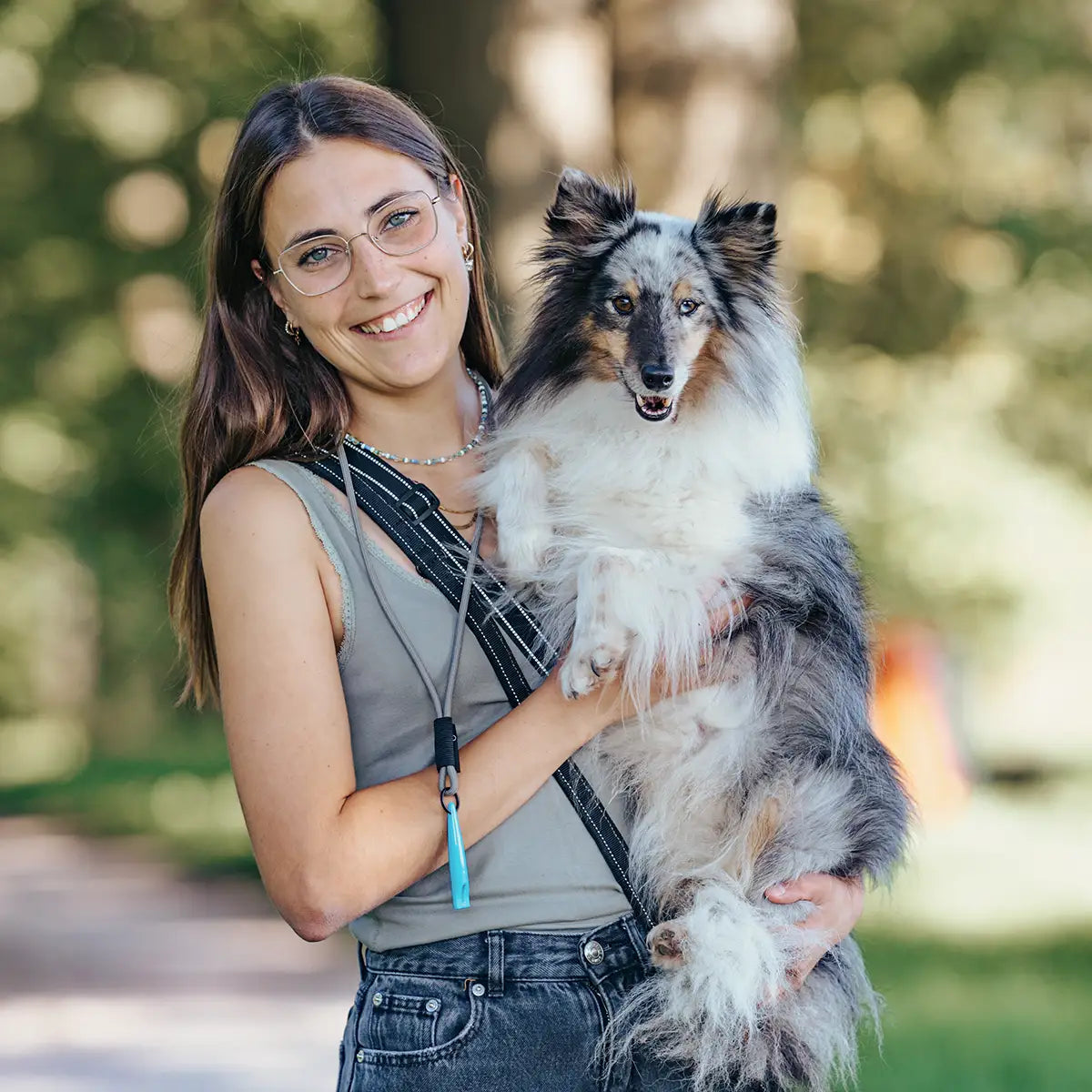 Frau trägt ihren Hund auf dem Arm, mit Hundepfeife und Futtertasche – praktische Trainingsausrüstung für unterwegs.