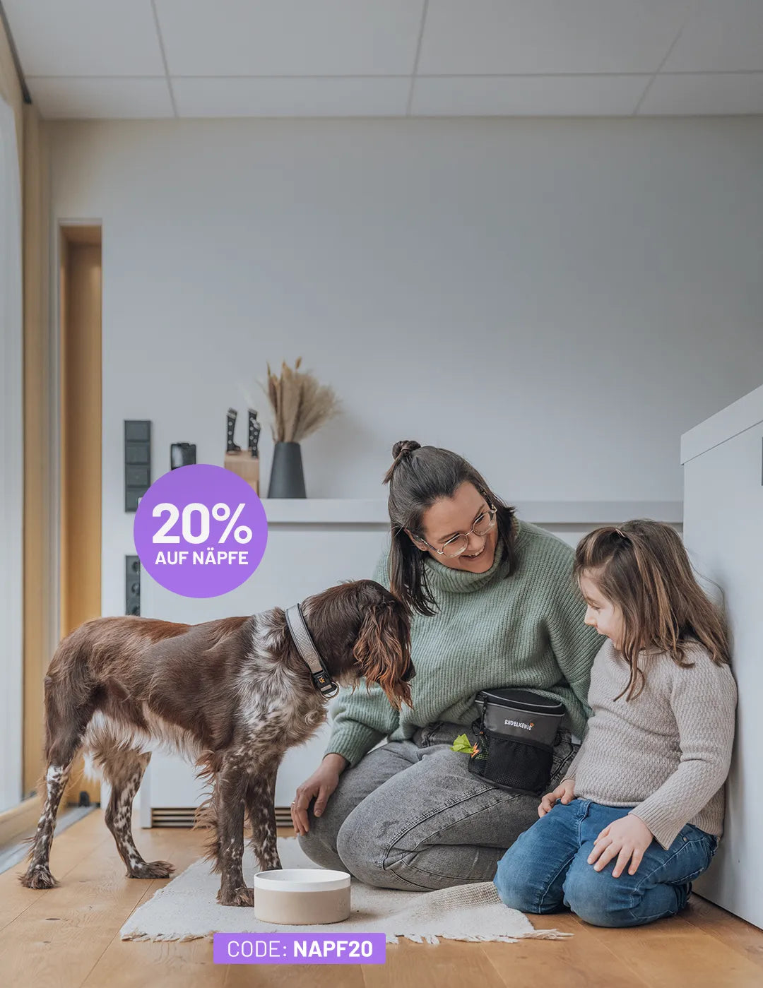 Näpfe mit 20% Rabatt, Code NAPF20: Hund mit gewelltem Fell steht vor dem Hundenapf, eine Frau mit Brille lächelt ihm zu.