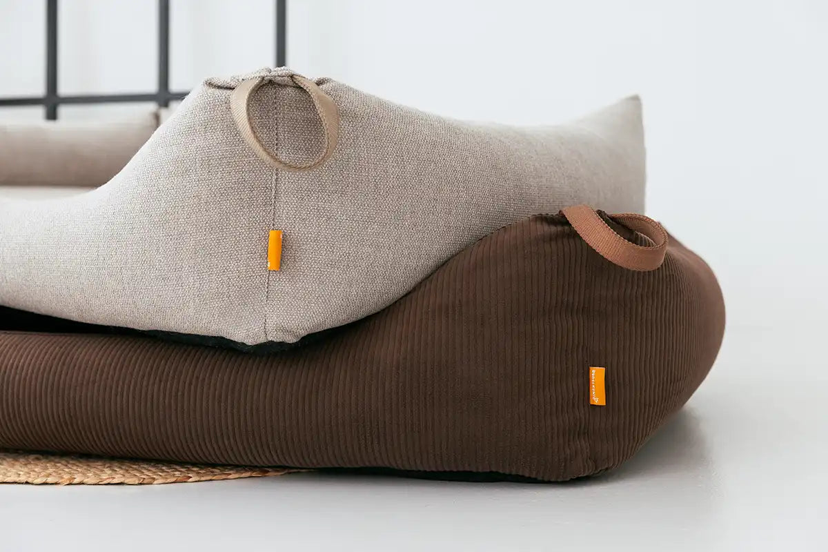 Die beiden Hundebetten Koye von Rudelkönig in Cord dunkelbraun und taupe Webstoff liegen aufeinander, man sieht die Schlaufen und das Logo.